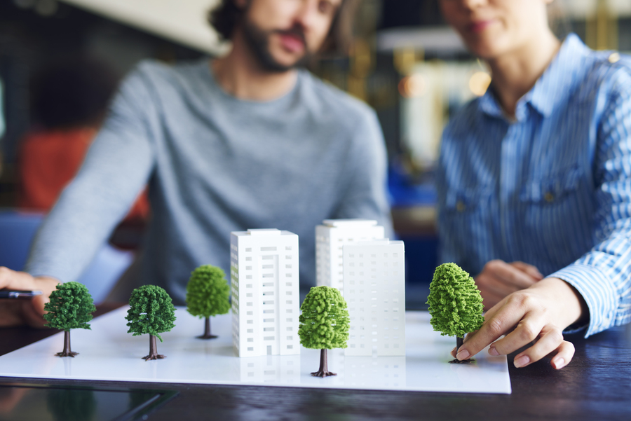 Arquitetos falando sobre construção sustentável enquanto mexem numa maquete com prédios e árvores em miniatura